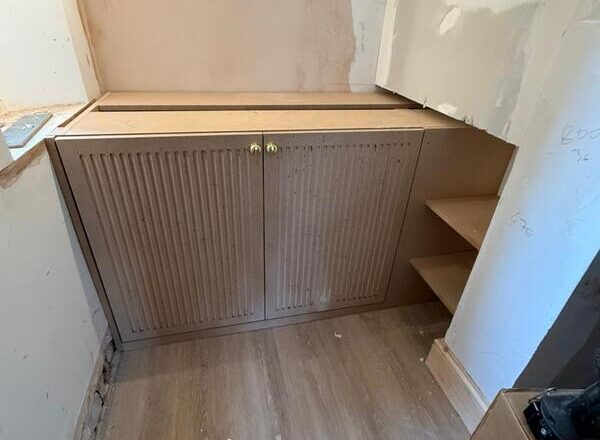 Fitted wine cabinet with fluted doors and brass knobs installed in a recessed alcove.
