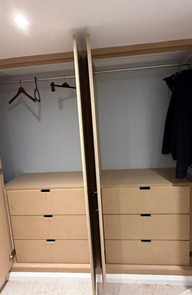 Open wardrobe showing hanging rails and integrated drawer units inside loft fitted storage.