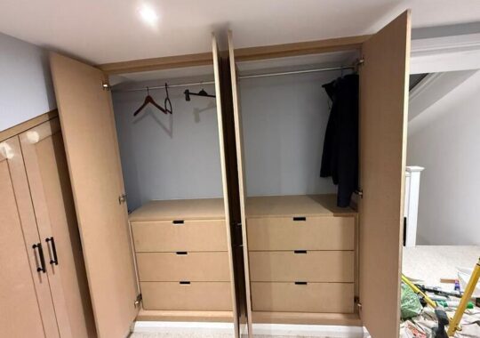 Open wardrobe showing hanging rails and integrated drawer units inside loft fitted storage.
