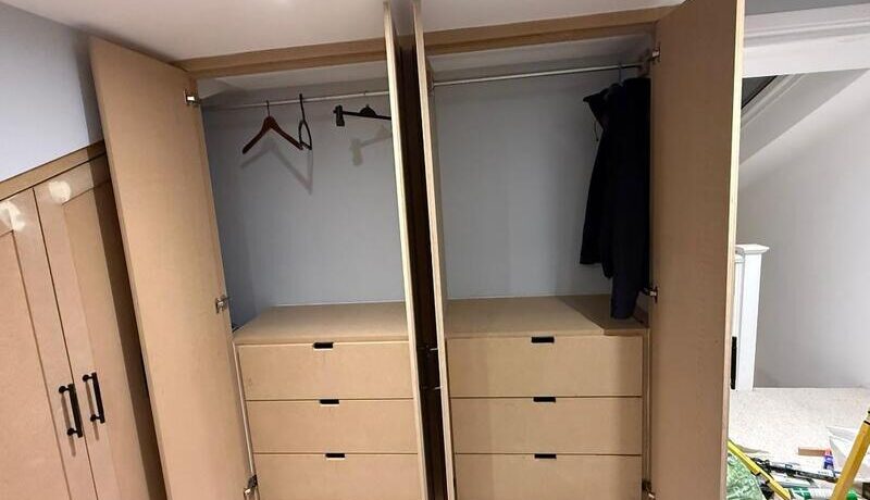 Open wardrobe showing hanging rails and integrated drawer units inside loft fitted storage.