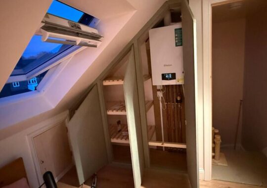 Open loft cabinet showing internal shelves and boiler access section with pipework.