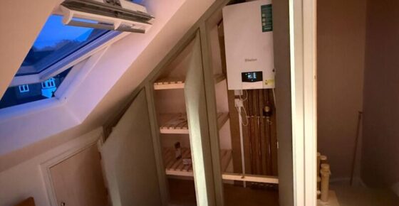 Open loft cabinet showing internal shelves and boiler access section with pipework.