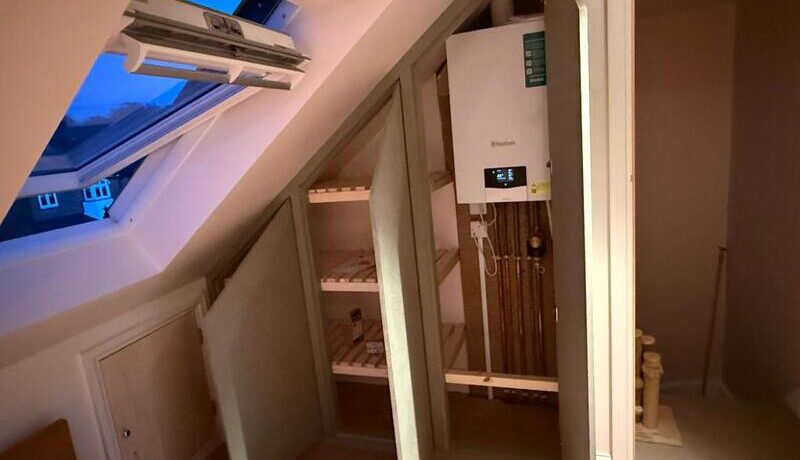 Open loft cabinet showing internal shelves and boiler access section with pipework.