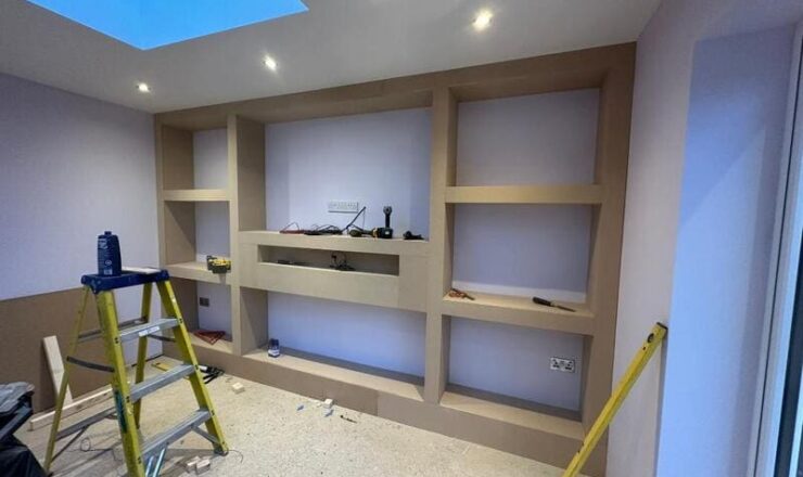 Media wall framework with built-in shelves and central TV recess during installation in Chigwell.