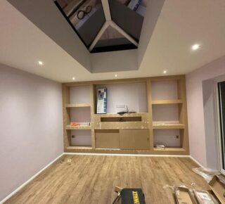Media wall framework with built-in shelves and central TV recess during installation in Chigwell.