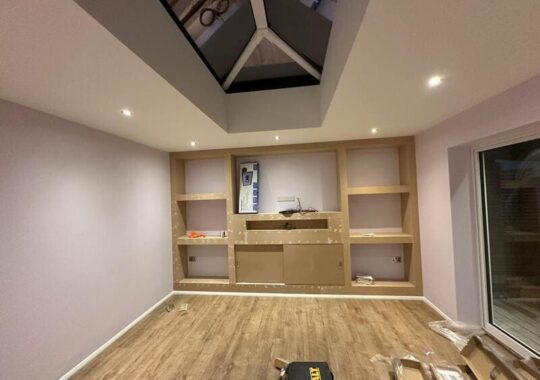 Media wall framework with built-in shelves and central TV recess during installation in Chigwell.
