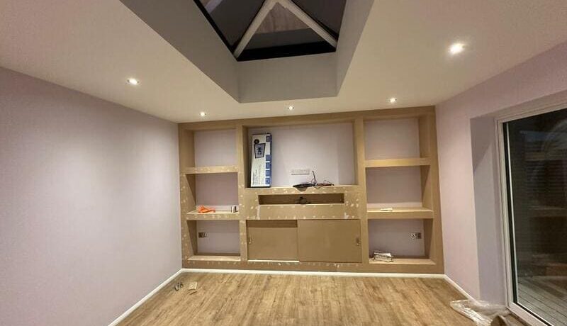 Media wall framework with built-in shelves and central TV recess during installation in Chigwell.
