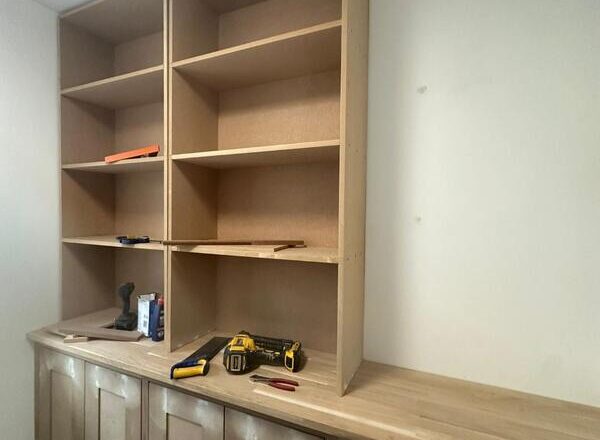 Upper bookshelf section installed above base cupboards with open shelving bays.