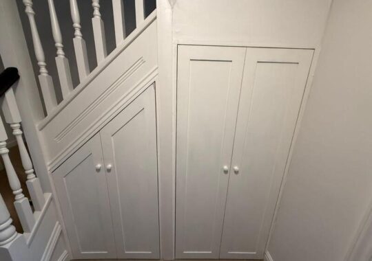 Completed under-stairs cupboards with white shaker doors and knobs, finished to match staircase.