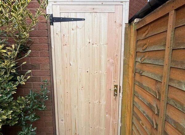 Timber side gate with black strap hinges and latch installed for secure access.