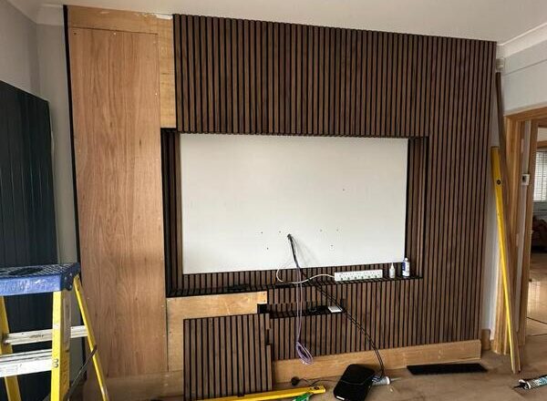 Slatted media wall installation in progress with recessed TV space and cable access