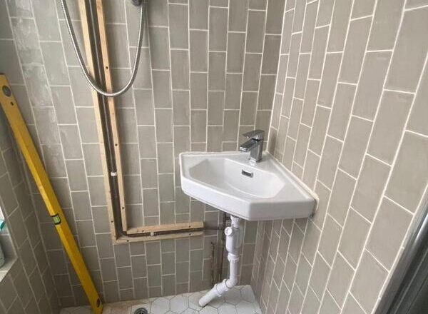 Corner basin with exposed pipework in shower room before vanity cabinet installation in Leytonstone.