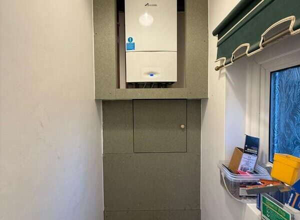 Boiler enclosure boarded with a large service access hatch and lower pipe opening.