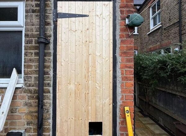New solid timber back door installed with black strap hinges in a brick rear entrance.