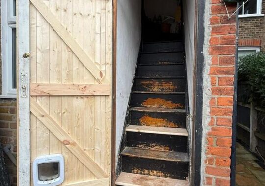 Open rear timber door showing access to interior staircase after refurbishment work.